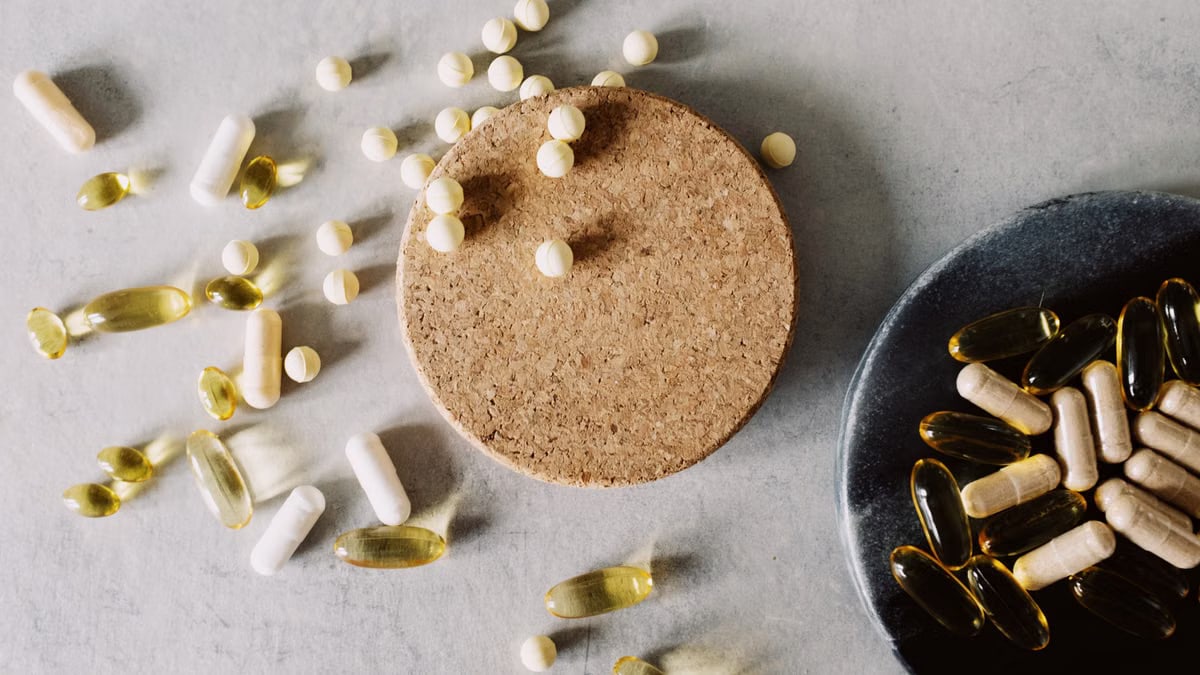 A variety of capsules and tablets scattered on a cork and plate, representing healthcare and wellness.